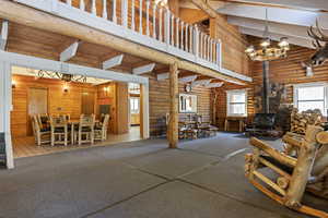 Living room featuring high vaulted ceiling, a wood stove, healthy amount of natural light, beam ceiling, and a chandelier