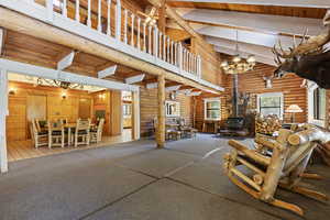 Living area with a wood stove, high vaulted ceiling, a chandelier, a wooden ceiling with exposed beams, and rustic walls