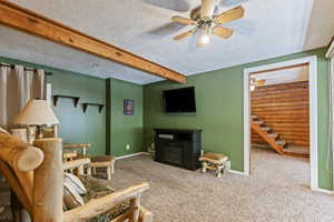 Carpeted living room featuring beamed ceiling, a textured ceiling, and ceiling fan