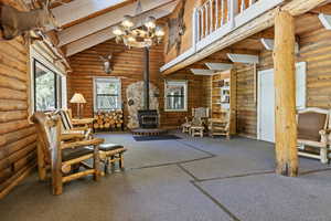 Living area with high vaulted ceiling, a wood stove, beam ceiling, carpet floors, and rustic walls