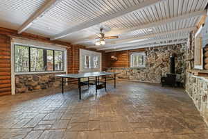 Recreation room with a wood stove, healthy amount of natural light, ceiling fan, and beamed ceiling