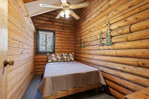 Carpeted bedroom with rustic walls, wooden ceiling, and ceiling fan