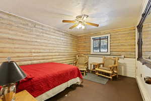 Bedroom featuring a textured ceiling, rustic walls, a ceiling fan, and concrete floors