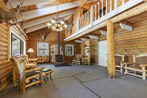 Living room with high vaulted ceiling, a wood stove, carpet, a wood ceiling with exposed beams, and rustic walls