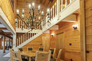 Dining space with a towering ceiling, wooden walls, stairs, a chandelier, and a wood stove