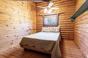 Bedroom featuring wood-type flooring, rustic walls, and ceiling fan