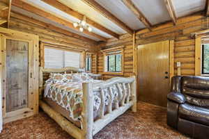 Bedroom with beamed ceiling, multiple windows, carpet, and rustic walls