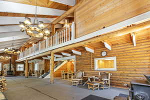 Common area with high vaulted ceiling, a wooden ceiling with exposed beams, stairway, log walls, and wood walls