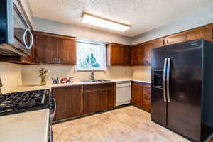 Kitchen with appliances with stainless steel finishes, light countertops, a textured ceiling, backsplash, and dark brown cabinets