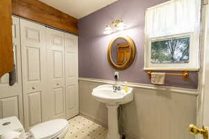Half bathroom with a wainscoted wall, a closet, and light floors