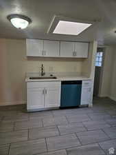 Kitchen with a textured ceiling, white cabinetry, dishwasher, wood finish floors, and a skylight