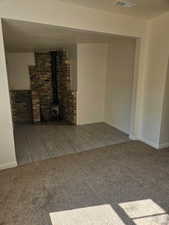 Unfurnished living room with a wood stove, carpet flooring, wood tiled floors, and brick wall