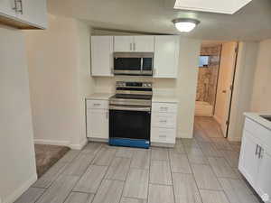 Kitchen with white cabinets, appliances with stainless steel finishes, a textured ceiling, and wood finish floors