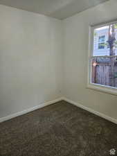 Spare room featuring dark colored carpet and baseboards