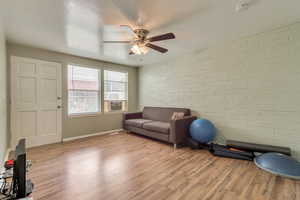 Exercise room with light wood-type flooring, brick wall, and ceiling fan