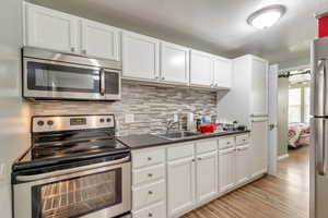 Kitchen featuring stainless steel appliances, white cabinets, dark countertops, decorative backsplash, and light wood-style floors