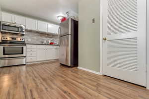 Kitchen with stainless steel appliances, white cabinets, dark countertops, light wood-style floors, and tasteful backsplash