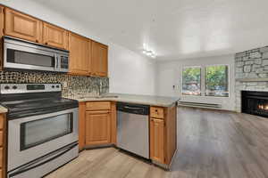 Kitchen featuring appliances with stainless steel finishes, a peninsula, tasteful backsplash, light stone countertops, and light wood-style floors
