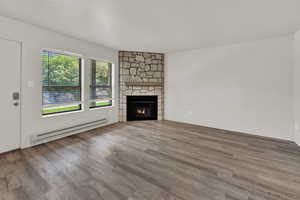 Unfurnished living room featuring a baseboard radiator, wood finished floors, a stone fireplace, and a textured ceiling