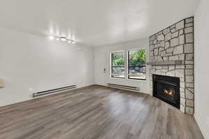 Unfurnished living room featuring a baseboard radiator, a stone fireplace, a textured ceiling, and wood finished floors