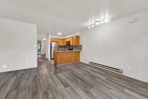 Kitchen with open floor plan, baseboard heating, backsplash, light countertops, and appliances with stainless steel finishes
