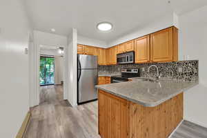 Kitchen featuring appliances with stainless steel finishes, light stone counters, light wood finished floors, and a peninsula