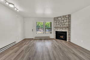 Unfurnished living room featuring a textured ceiling, a stone fireplace, light wood finished floors, and baseboard heating