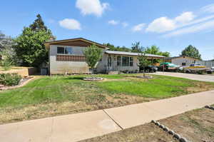 Split level home featuring driveway, brick siding, an attached carport, and a front yard