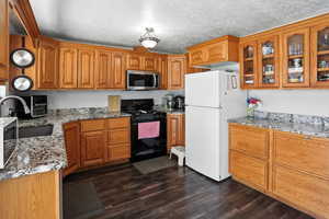 Kitchen featuring black range with gas cooktop, light stone countertops, freestanding refrigerator, stainless steel microwave, and a textured ceiling