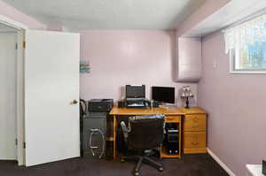 Home office featuring dark colored carpet and a textured ceiling