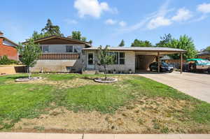 Split level home with brick siding, a carport, driveway, and a front yard