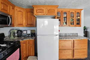Kitchen with black gas range oven, freestanding refrigerator, dark stone counters, a textured ceiling, and stainless steel microwave