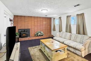 Living area featuring a wood stove, a textured ceiling, and dark carpet