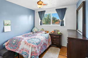 Bedroom with wood finished floors, a textured ceiling, and a ceiling fan