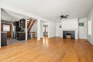 Living room featuring healthy amount of natural light, stairs, light wood-style flooring, and a tile fireplace