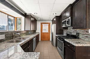 Kitchen with stainless steel appliances, dark brown cabinets, granite countertops, backsplash, and recessed lighting