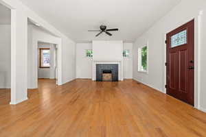 Living room featuring a fireplace, light wood-type flooring, plenty of natural light, and a ceiling fan