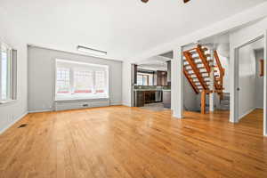 Living room, dining area with stairway, light wood finished floors, and ceiling fan