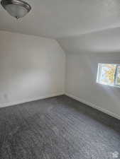 Bonus room with lofted ceiling, a textured ceiling, and dark carpet