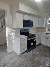Kitchen featuring white cabinets, stainless steel electric stove, wood finish floors, light countertops, and a textured ceiling