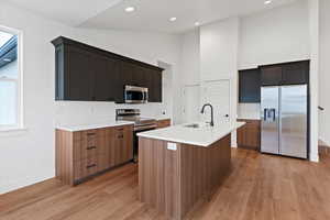 Kitchen featuring vaulted ceiling, stainless steel appliances, a center island with sink, light wood-style floors, and light stone countertops