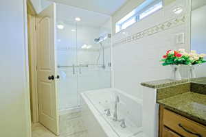 Full bath featuring a stall shower, a tub with jets, vanity, and light tile patterned flooring