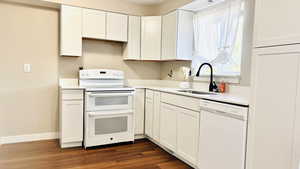Kitchen featuring white appliances, white cabinetry, dark wood-style floors, and light stone counters