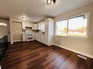 Kitchen featuring white cabinets, white appliances, light countertops, a textured ceiling, and dark wood-style floors