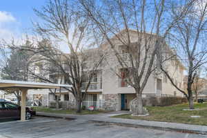 View of front facade with stone siding and covered and uncovered parking