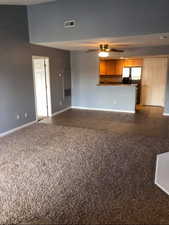 Unfurnished living room featuring dark tile patterned floors, dark colored carpet, and ceiling fan