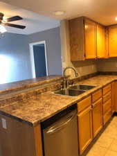 Kitchen with stainless steel dishwasher, a peninsula, light tile patterned floors, dark countertops, and a ceiling fan