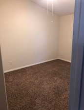 Spare room featuring dark colored carpet and baseboards