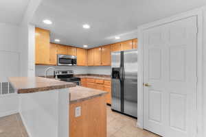 Kitchen featuring stainless steel appliances, recessed lighting, a peninsula, light tile patterned floors, and a kitchen bar