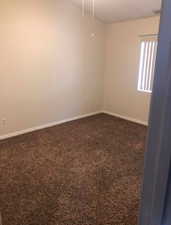 Unfurnished room featuring dark carpet and baseboards